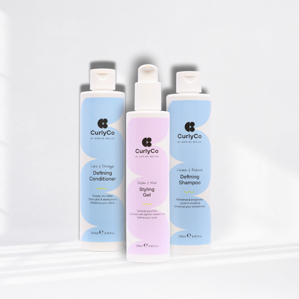 Four curly hair care products from CurlyCo, including shampoo, conditioner, cream, and mousse.